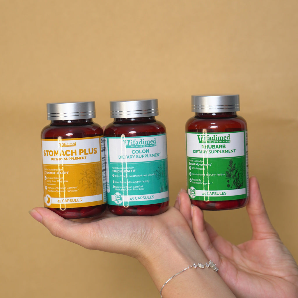 Three Vifadimed digestive supplement bottles labeled 'Stomach Plus', 'Colon', and 'Rhubarb' held by a hand against a beige background.