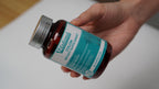 Hand holding a bottle of a dietary supplement with a white background