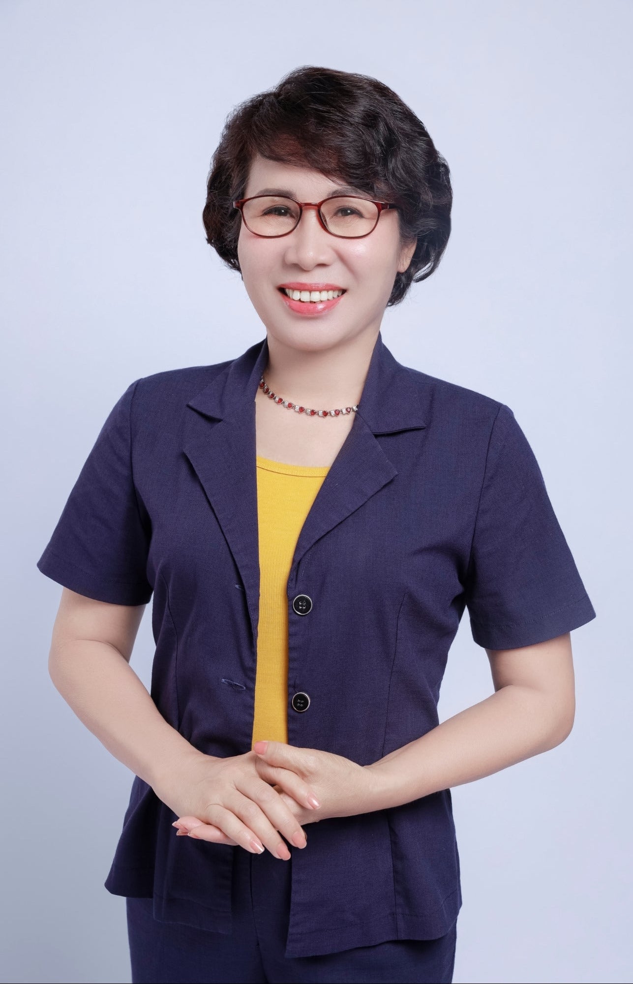 Woman wearing a navy blue blazer over a yellow top against a light gray background